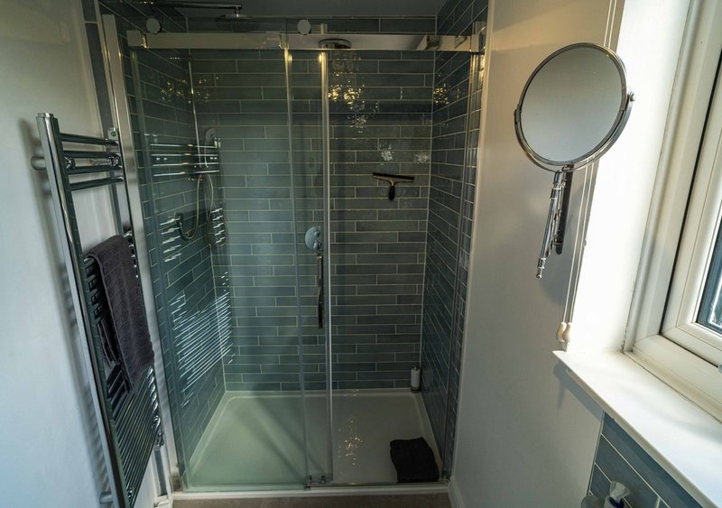 Modern bathroom with dark green tile shower enclosure, heated towel rack, and circular mirror
