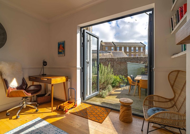 Bright home office with desk, chair, and wicker seating overlooking garden patio