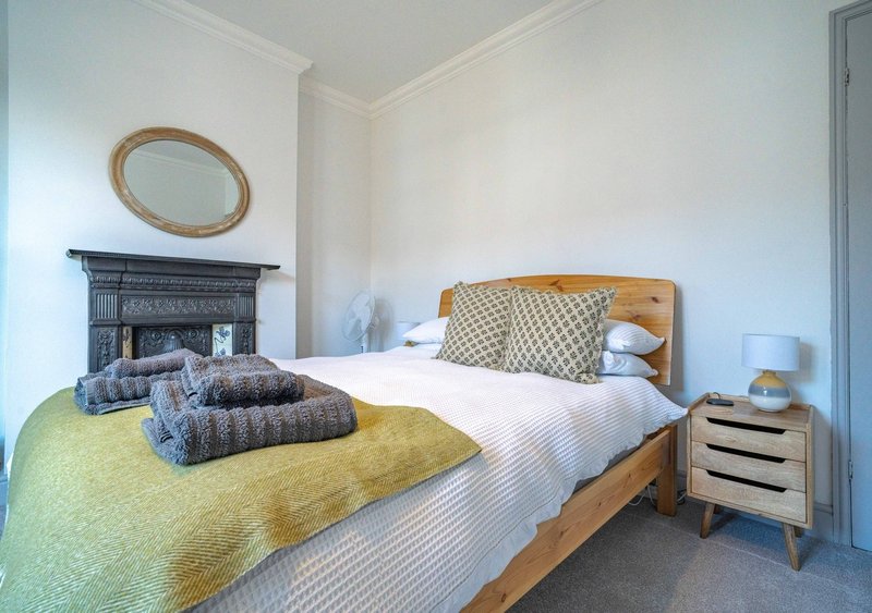 Bright bedroom with wooden bed, yellow bedding, fireplace and oval mirror