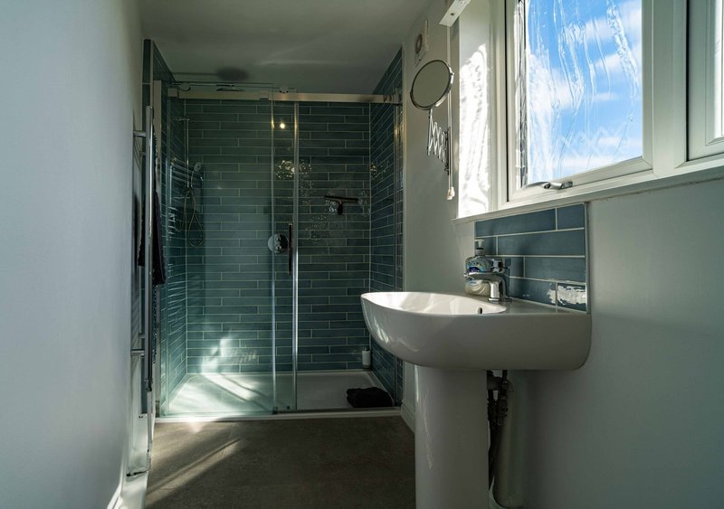 Modern bathroom with walk-in shower, pedestal sink, and window with natural light