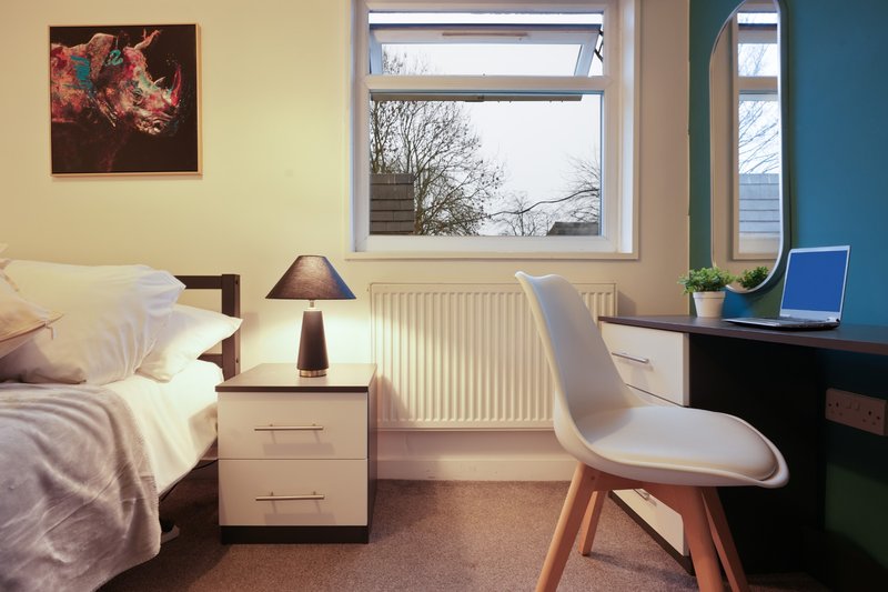 Bedroom with bed, desk, chair, bedside lamp and windows overlooking garden