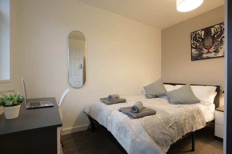 Modern bedroom with double bed, grey bedding, wall mirror, desk with laptop and plant