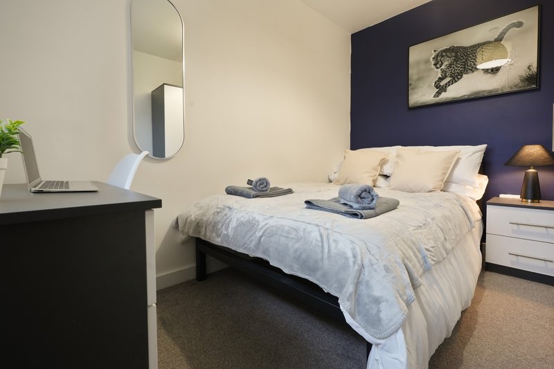 Modern bedroom with double bed, navy accent wall, desk, and framed artwork