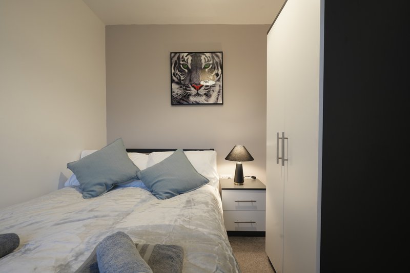 Compact bedroom with double bed, blue pillows, bedside table with lamp and framed wall art