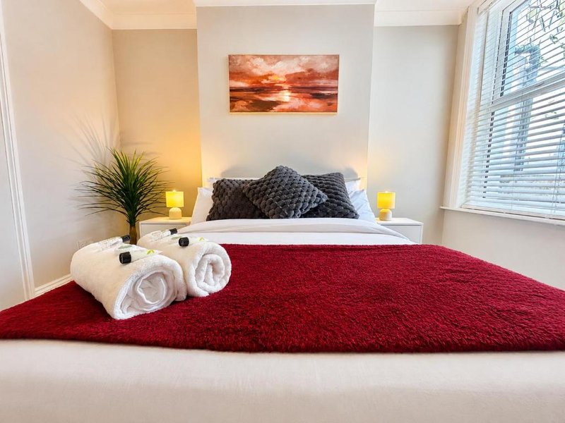Modern bedroom with double bed, red rug, rolled towels, decorative pillows and bedside lamps
