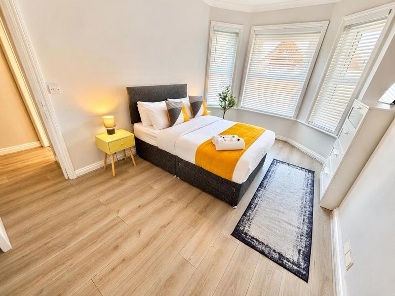 Modern bedroom with double bed, yellow side table, lamp, and bay windows with shutters
