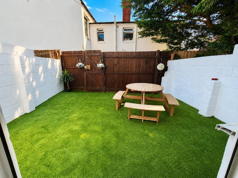 Outdoor patio area with artificial turf, wooden picnic table and cushioned seating