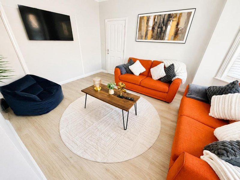 Modern living room with orange sofas, round white rug, wooden coffee table and wall-mounted TV