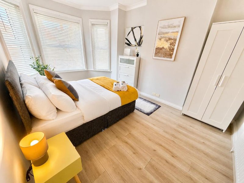 Bright modern bedroom with double bed, yellow accents, wooden flooring and large windows