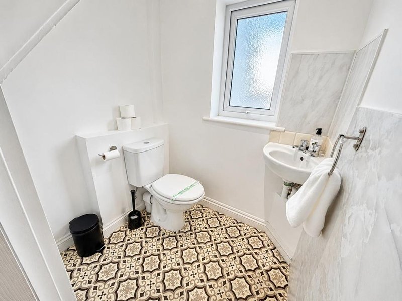 Small bathroom with toilet, sink, window and patterned tile flooring
