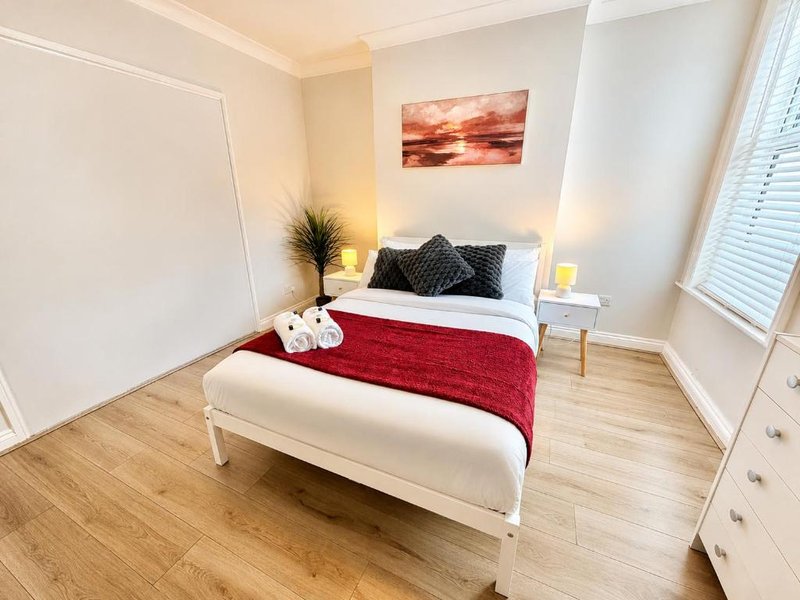 Bright bedroom with white bed, red bedding, sunset artwork, wooden floor and window