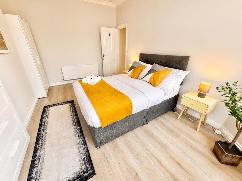 Bright bedroom with double bed, yellow bedding, wooden floor and potted plant