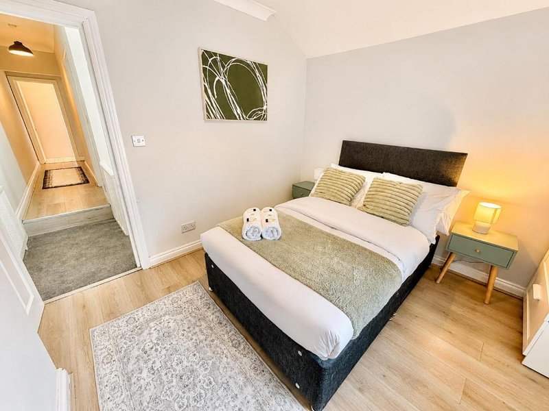 Bright bedroom with double bed, wooden floor, bedside table with lamp and ensuite bathroom visible