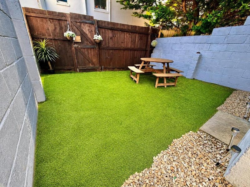 Enclosed back garden with artificial grass, wooden picnic table, and brown wooden fence