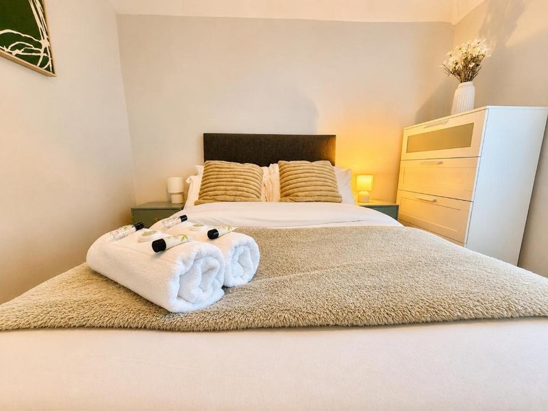 Bright bedroom with double bed, rolled towels, yellow cushions and wooden furniture