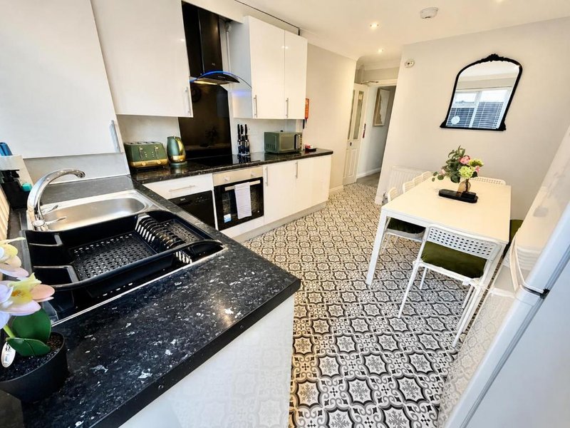 Modern kitchen with white cabinetry, black countertops, and patterned floor tiles extending into dining area