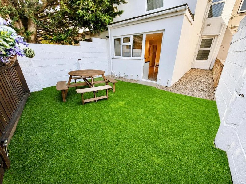 Rear garden with artificial grass, wooden picnic table, and modern white extension