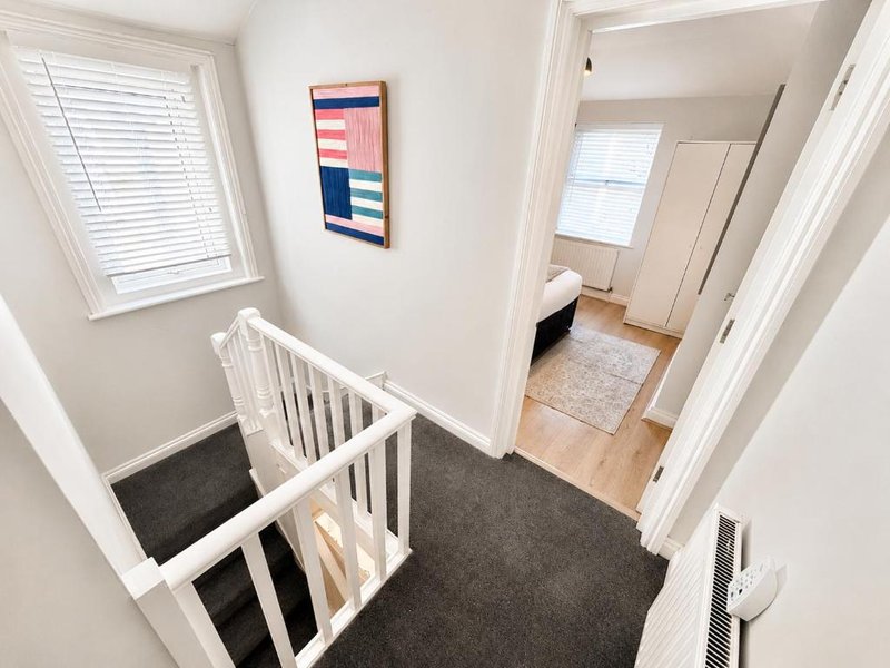 Hallway with staircase, white railings, wooden flooring, and abstract wall art