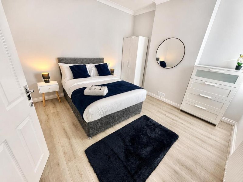 Modern bedroom with double bed, navy bedding, wooden flooring, white furniture and circular mirror