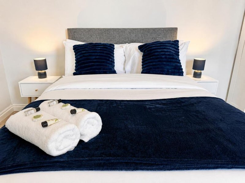 Modern bedroom with dark blue bedding, white pillows, gray headboard and folded towels on bed