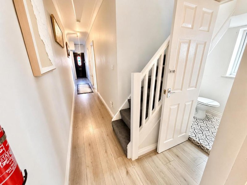 Bright hallway with wooden flooring, white walls, staircase with black railing and multiple white doors