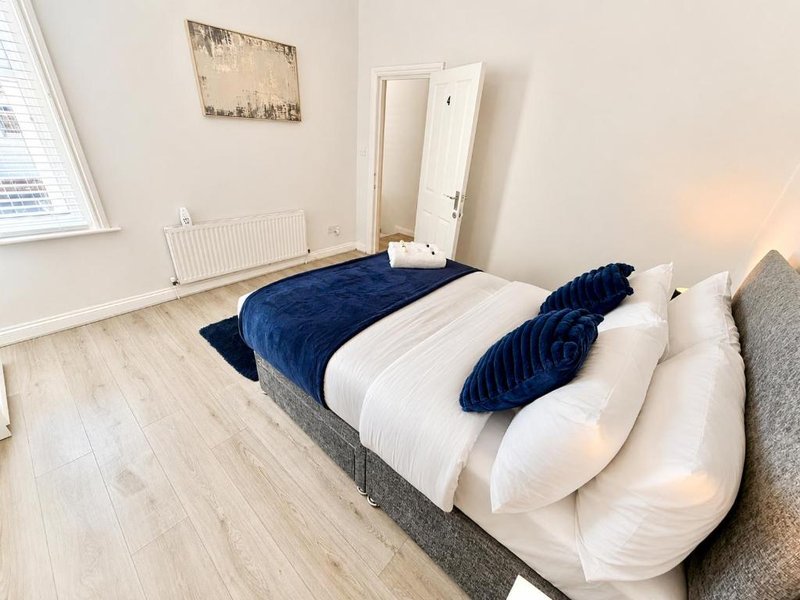 Bright bedroom with white bed, blue cushions, wooden floor and radiator