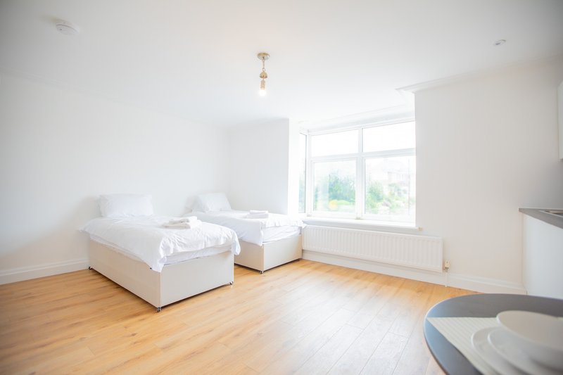 Bright bedroom with two single beds, wooden floor, large window and radiator