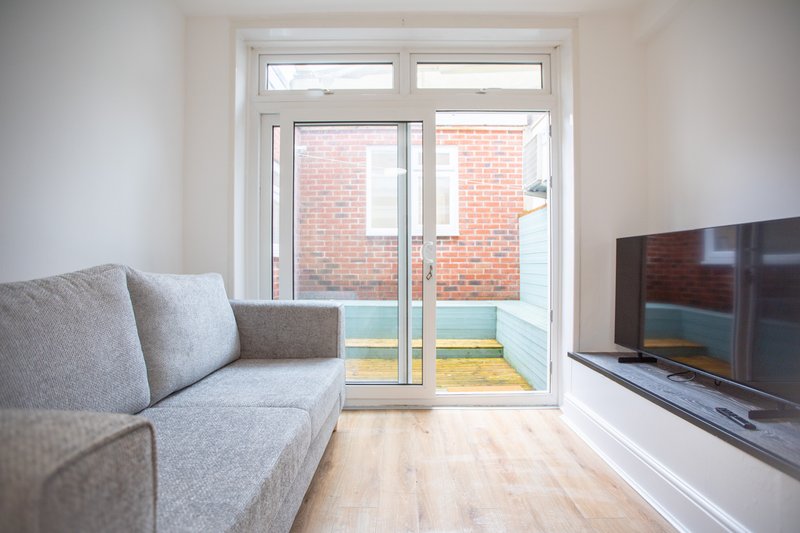 Bright living room with grey sofa, wooden floor, TV unit and French doors to garden