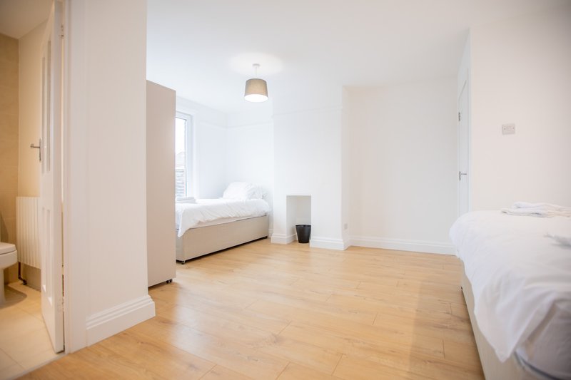 Bright studio apartment with wooden flooring, two beds, pendant light and white walls