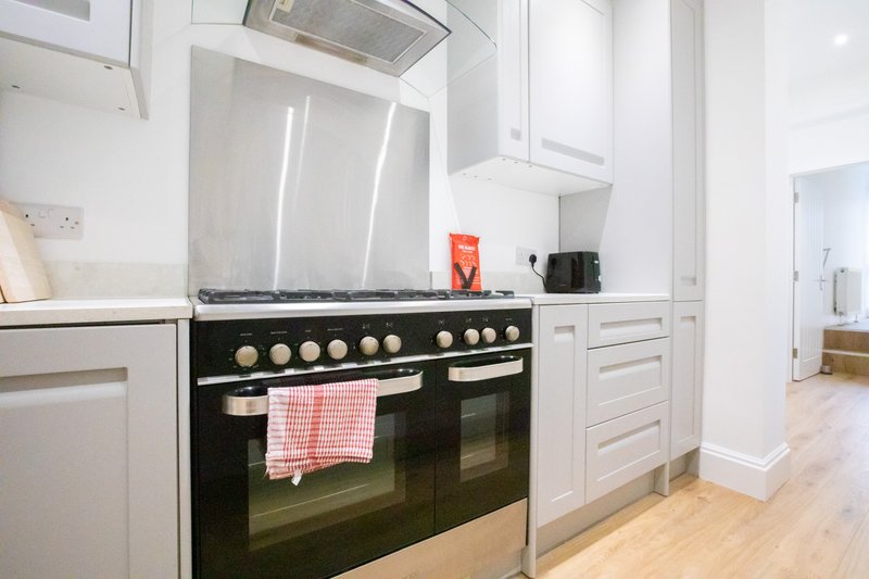 Modern kitchen with black range cooker, white cabinetry, stainless steel hood, and wooden flooring