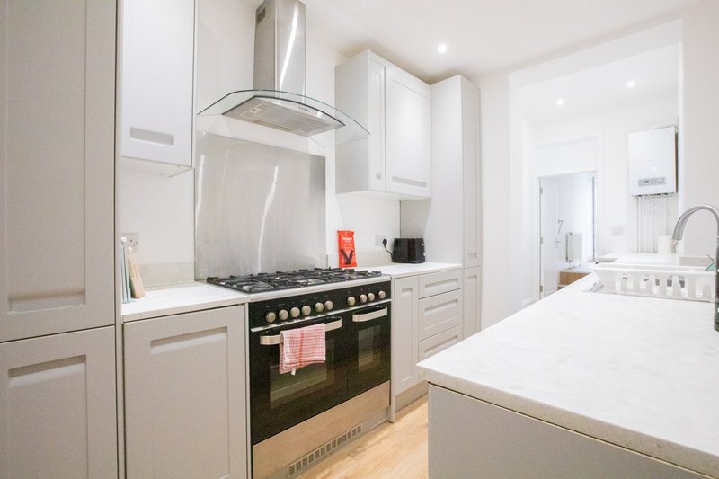 Modern kitchen with white cabinetry, black range cooker, island counter and stainless steel hood