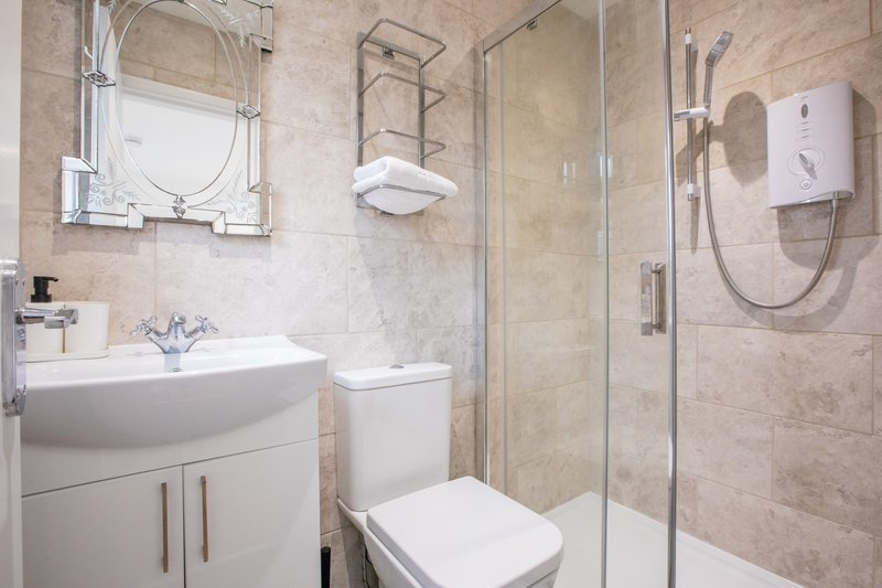 Modern bathroom with curved sink vanity, toilet, glass shower enclosure and heated towel rail