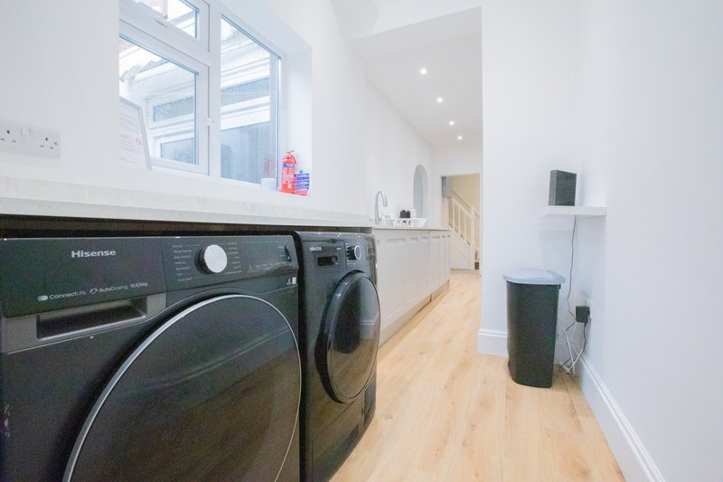 Modern laundry room with black washing machines, wooden floor, white walls and window