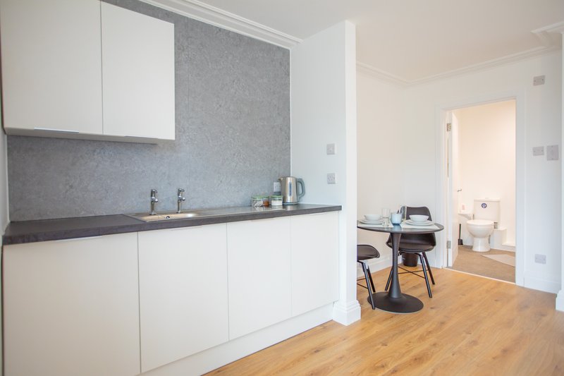 Modern kitchen with white cabinetry, grey tiled backsplash, wooden flooring, and view to dining area