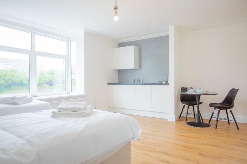 Bright modern bedroom with double bed, kitchenette, dining area and large window
