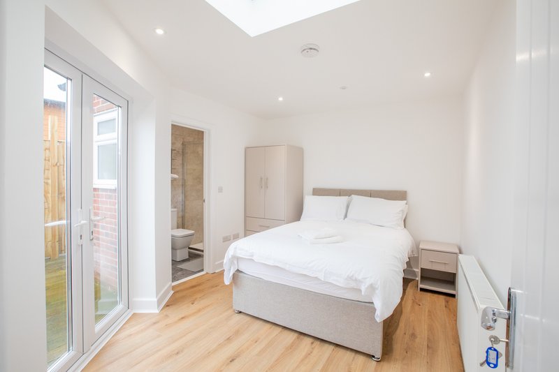 Bright modern bedroom with double bed, wooden flooring, patio doors and ensuite bathroom access