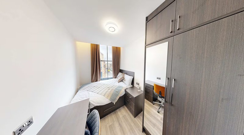 Compact bedroom with single bed, large wardrobe, wooden flooring and window with curtains