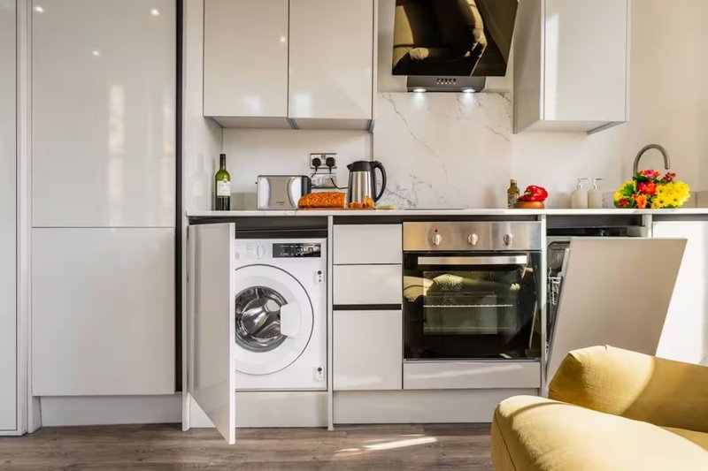 Modern kitchen with white cabinetry, integrated appliances, washing machine and oven visible