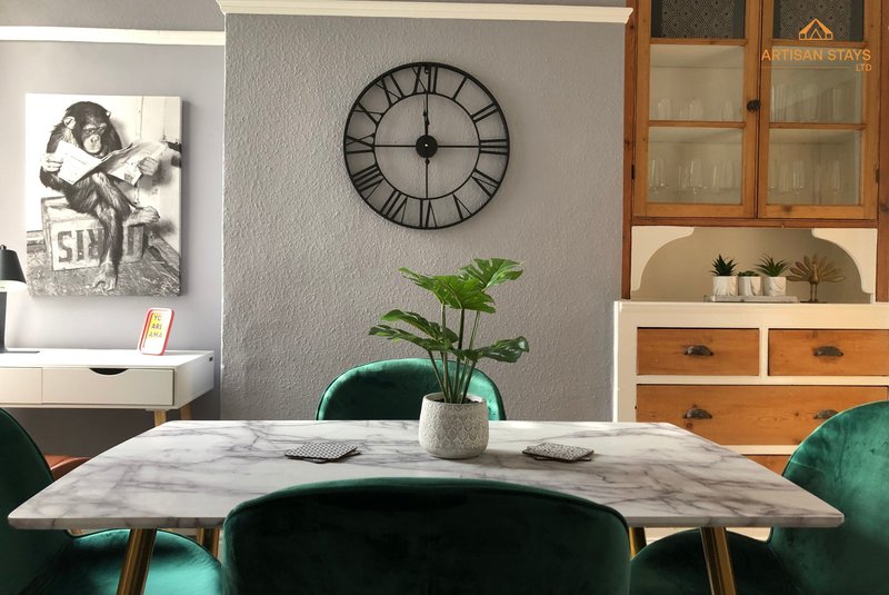 Dining area with marble table, green velvet chairs, wall clock, and potted plant