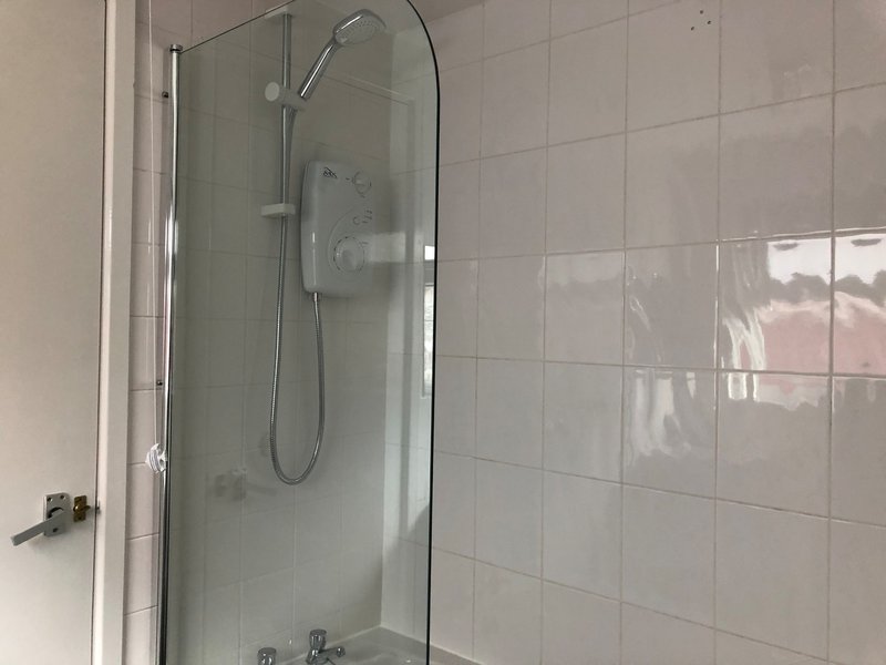 Clean bathroom with glass shower enclosure, white tile walls and showerhead