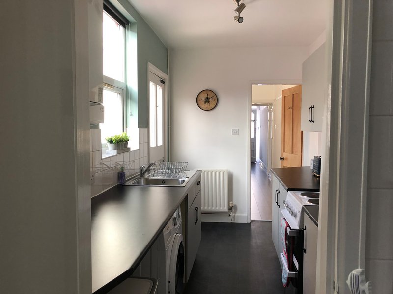 Galley kitchen with white cabinetry, dark countertops, washing machine and window with plant