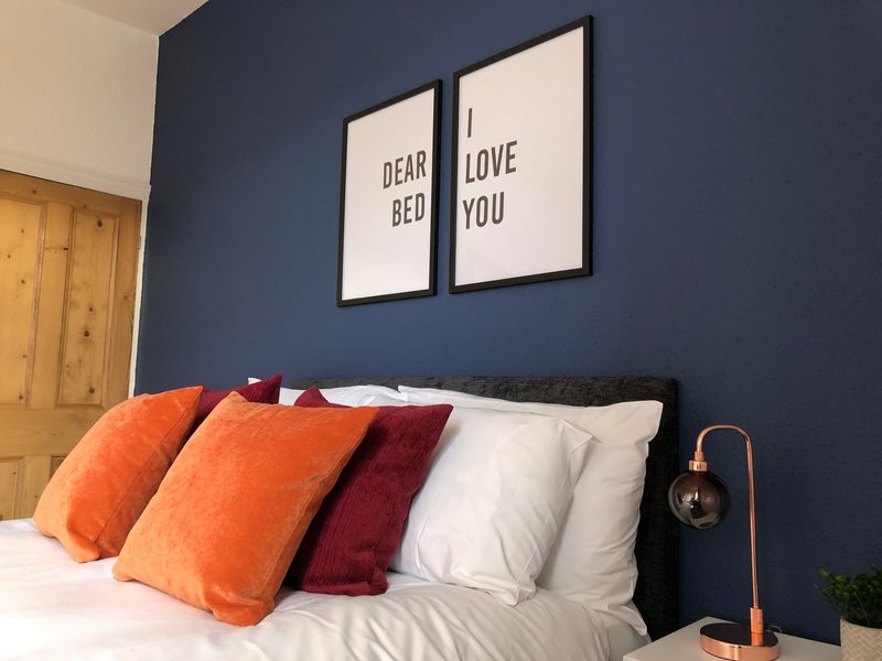 Bedroom with dark blue wall, black bed frame, colorful pillows and framed wall art