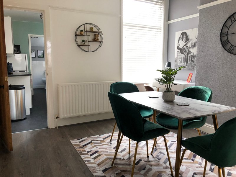 Modern dining area with white table, green velvet chairs, wall clock and potted plant