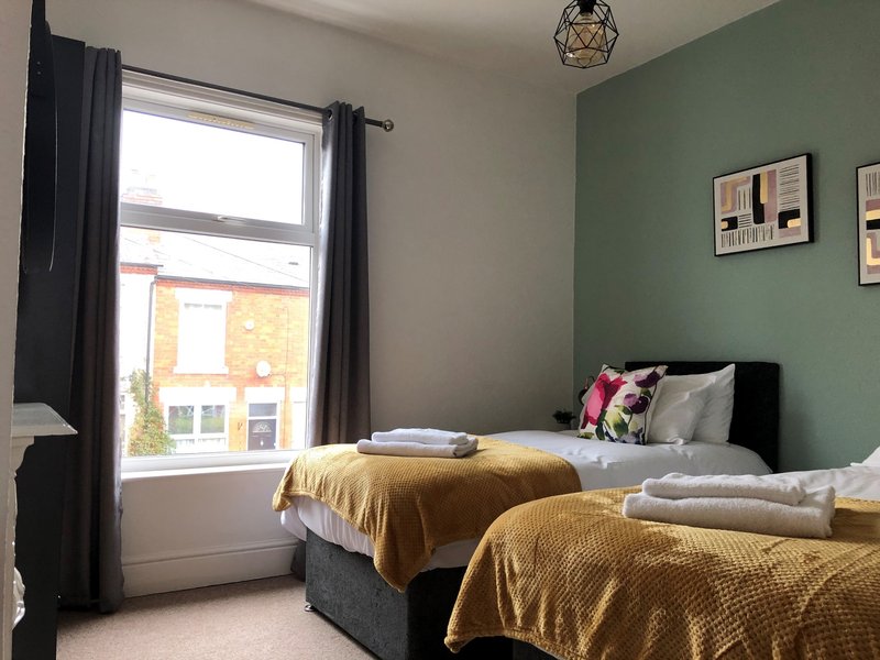 Bedroom with two beds, mustard throws, green accent wall, window with black curtains
