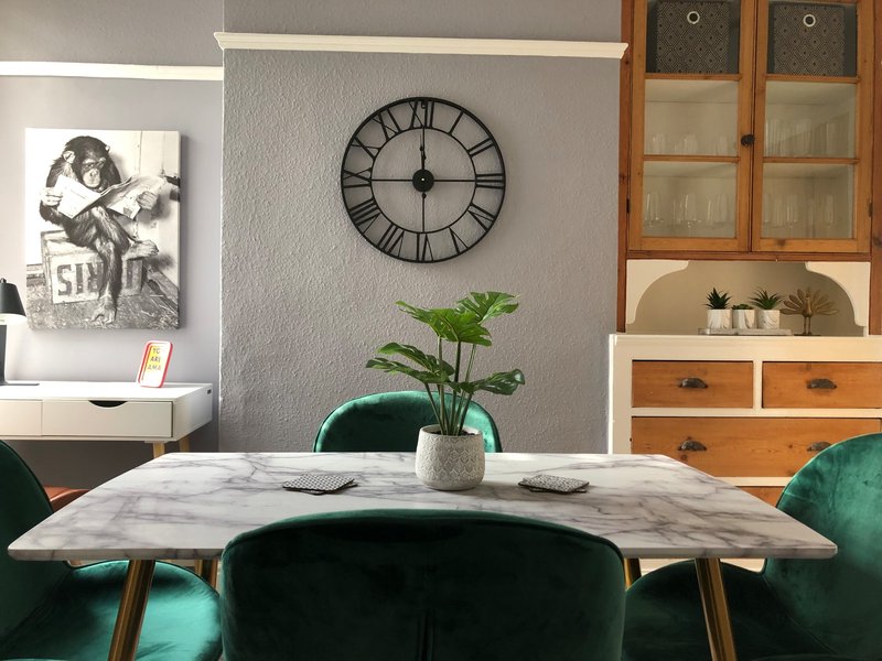 Dining area with marble table, green velvet chairs, wall clock, and wooden storage cabinet