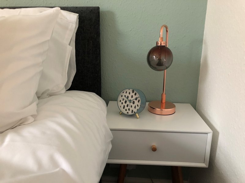 Bedroom nightstand with lamp, decorative objects and white bedding visible