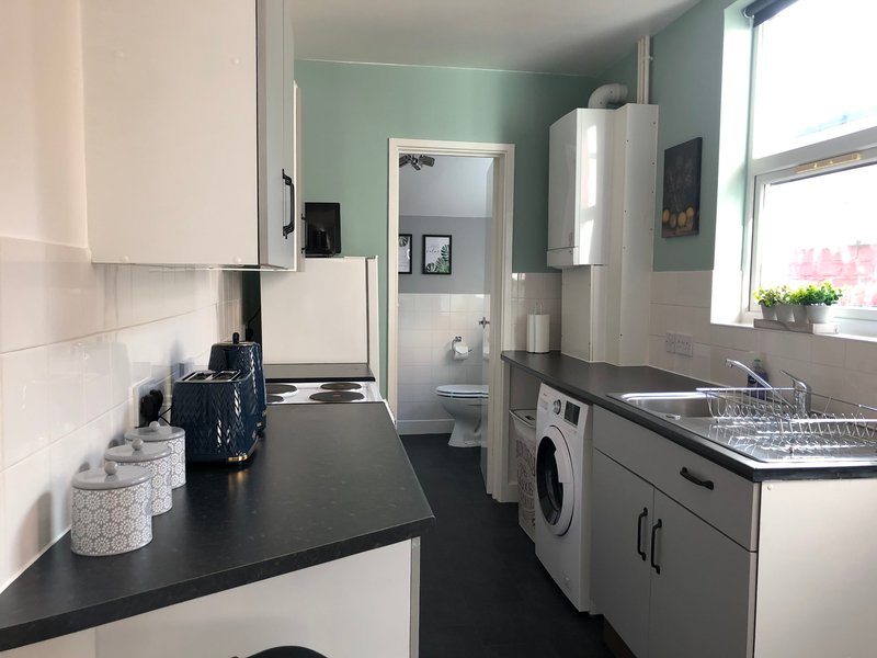Modern kitchen with white cabinetry, black countertop, washing machine, and window with plants