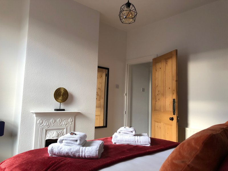 Bedroom with red bedding, white towels, fireplace mantle, wooden door and pendant light