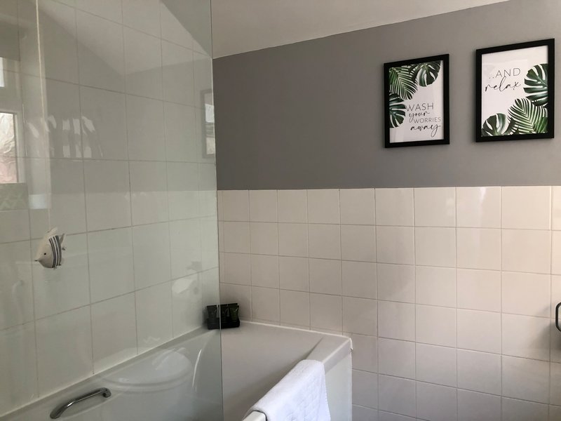 Bathroom with white subway tiles, glass shower enclosure, white bathtub, and botanical wall art