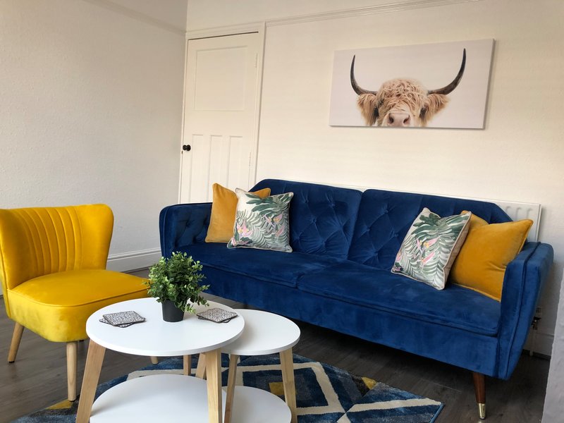 Living room with blue velvet sofa, yellow accent chair, white coffee table and wall art